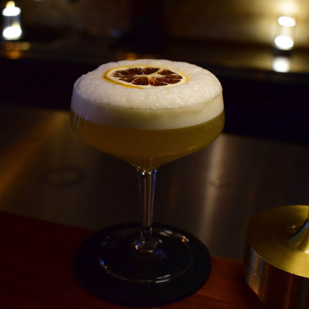 Cocktail with foam and a lemon wheel on a bar with candles in the background