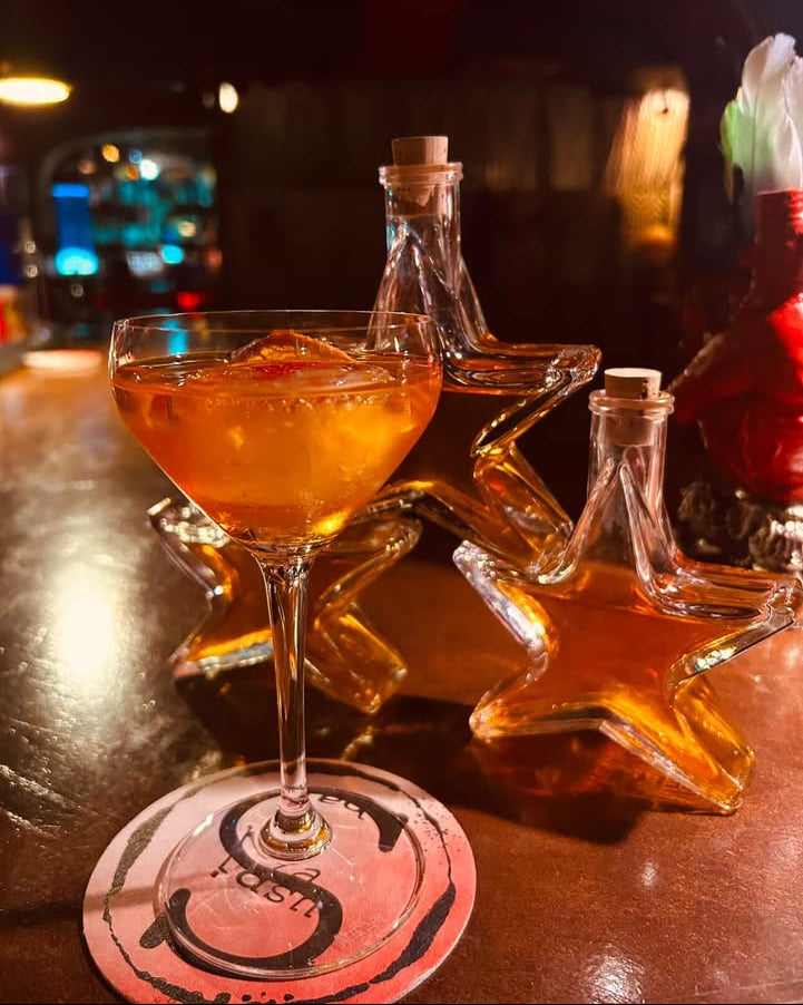 Glass of orange cocktail with star-shaped bottle on a bar counter