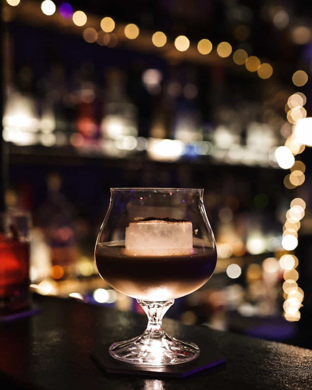 Glass of dark liquid on a bar counter with blurred lights in the background